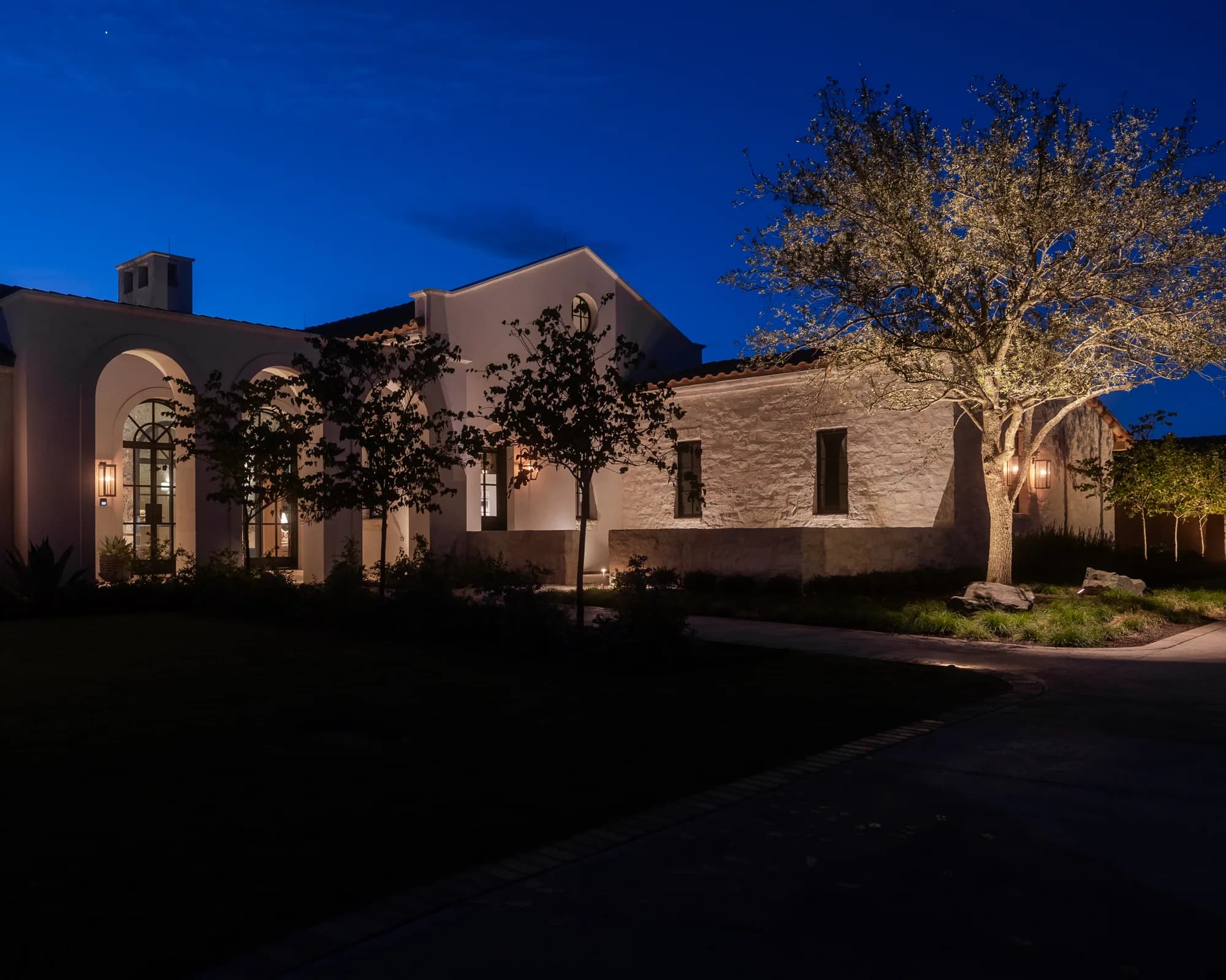 Forrest Jr. estate in Texas with illuminated stone walls and trees beneath a blue evening sky